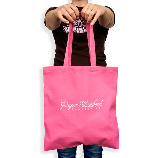 Pink cotton canvas tote bag with floral G logo held by woman with arms extended in front of body on white background
