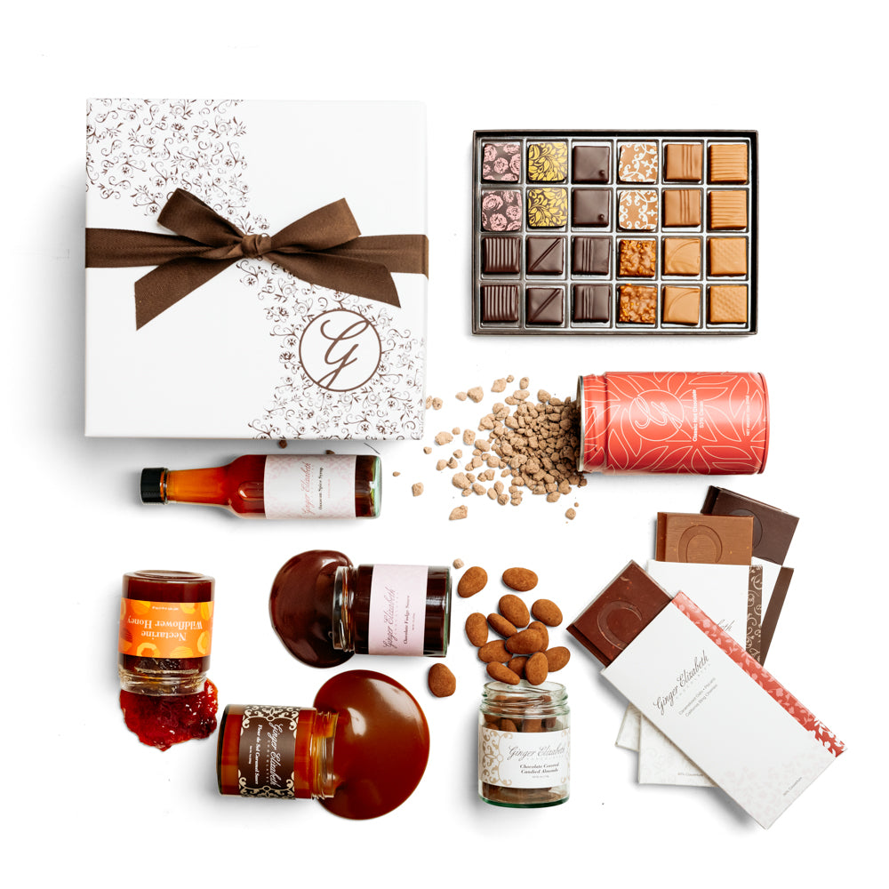 Gift Box shown with 24 piece assorted chocolate bonbon box, 3 chocolate dessert bars, classic hot cocoa tin, chocolate covered almonds, fudge sauce, fleur de sel caramel sauce, artisanal jam and oaxacan spice syrup arranged on white background.