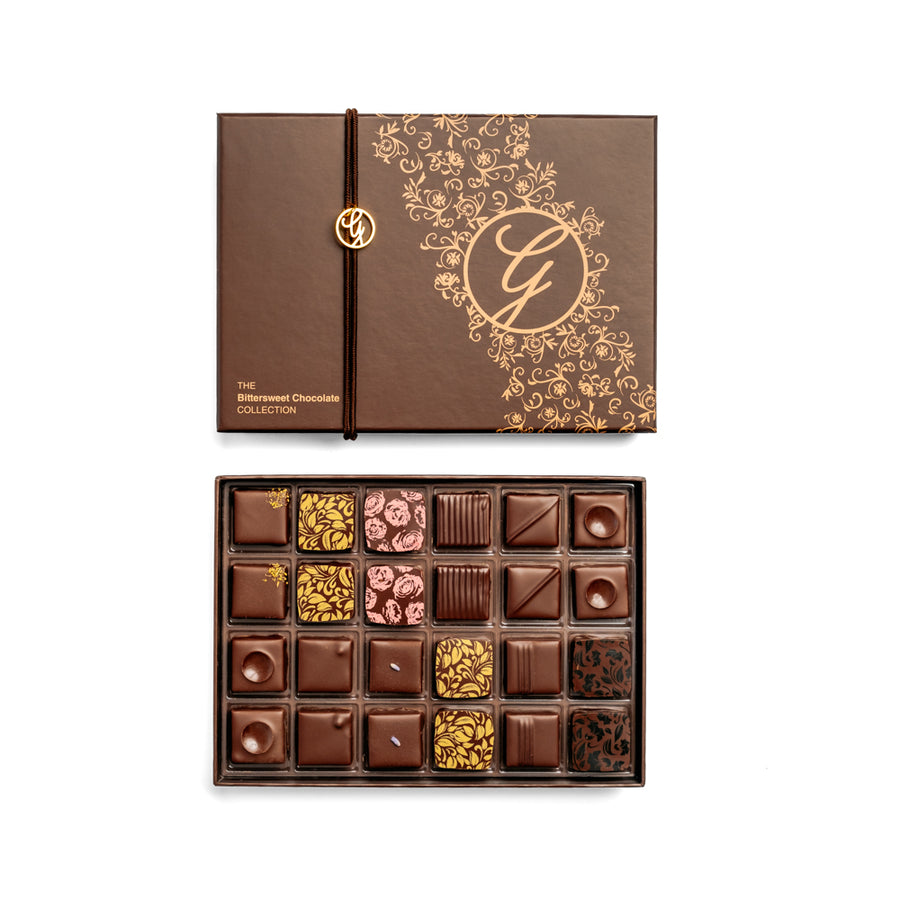 open 24-piece box of dark chocolate bonbons arranged under closed box on white background