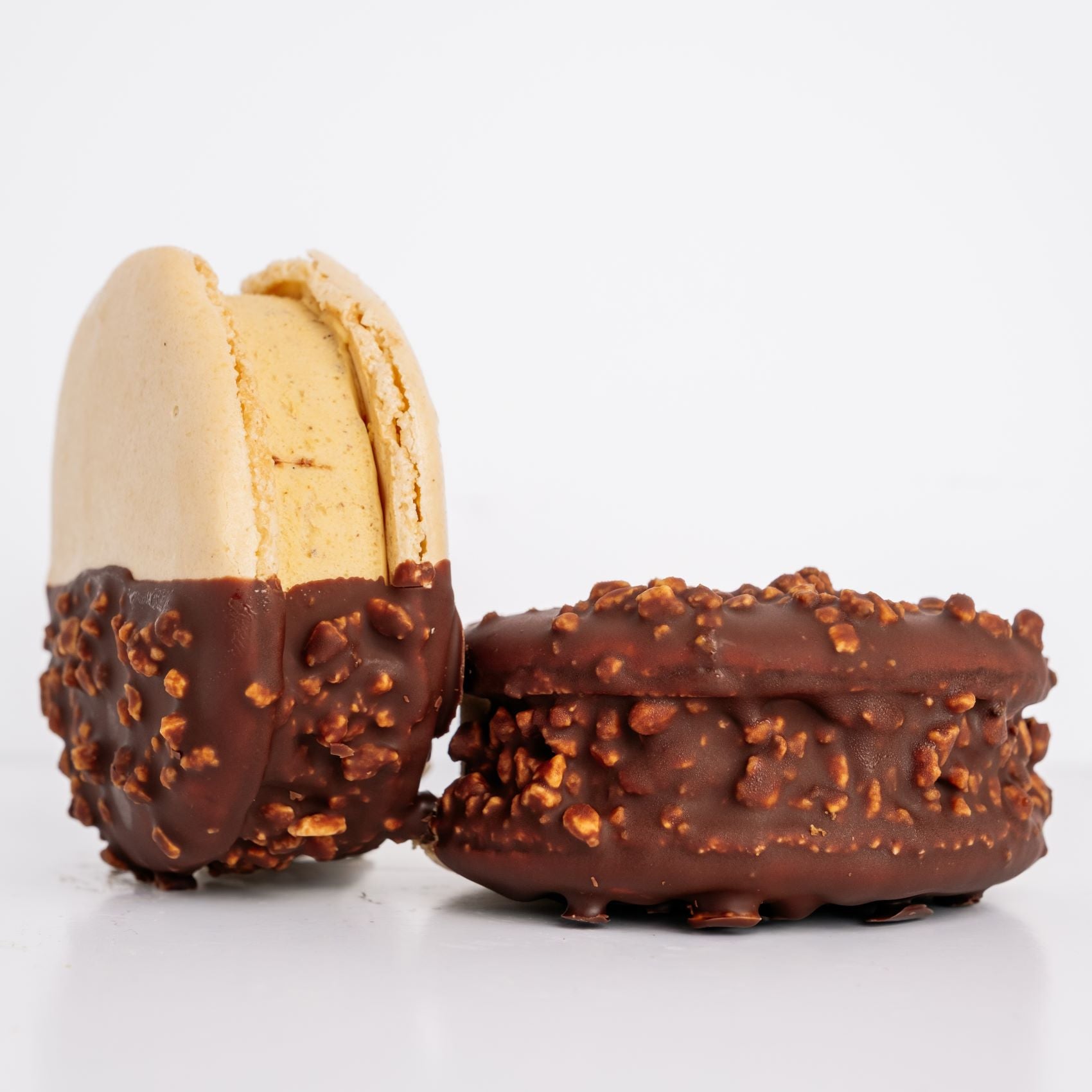 Two chocolate-dipped macaron ice cream sandwiches with a white background