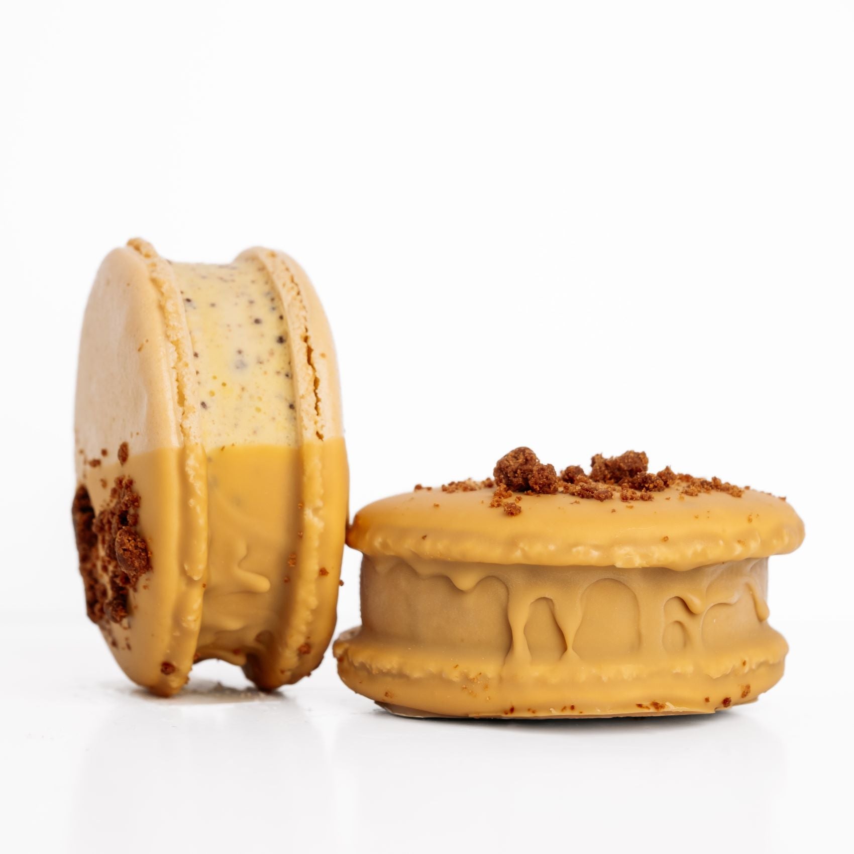 Two white chocolate dipped macaron ice cream sandwiches with a crumbly topping on a white background