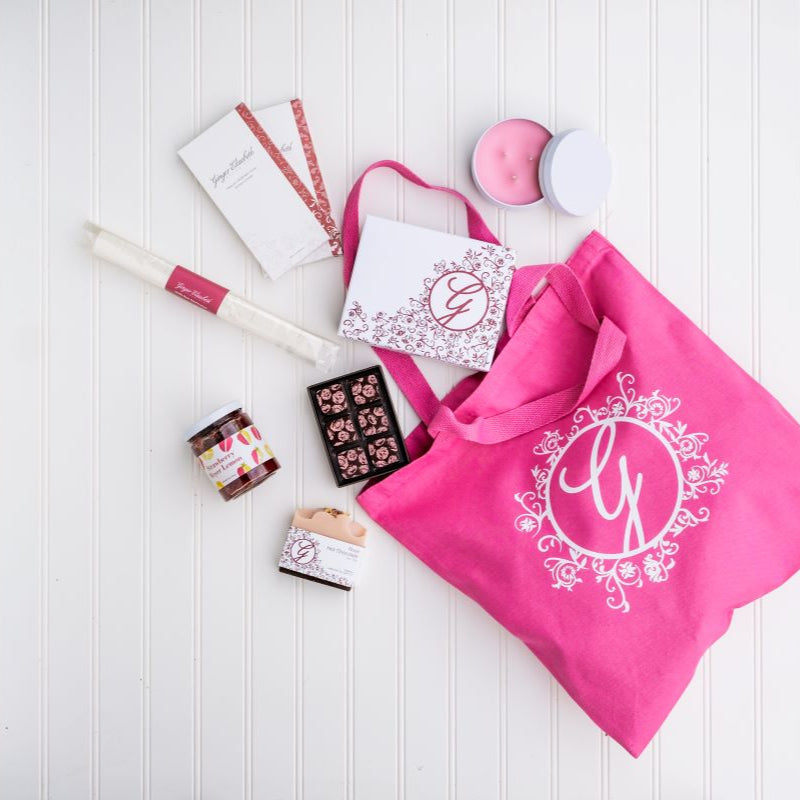 Pink cotton canvas tote bag with floral G logo on white background with packaged Chocolates, candle, soap, marshmallow baton, jam and chocolate bars