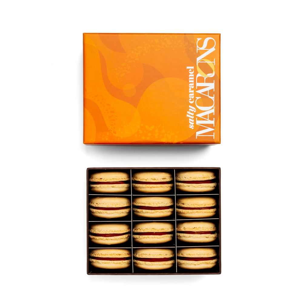 Open 12 piece box of salty caramel macarons with new caramel colored lid above on white background