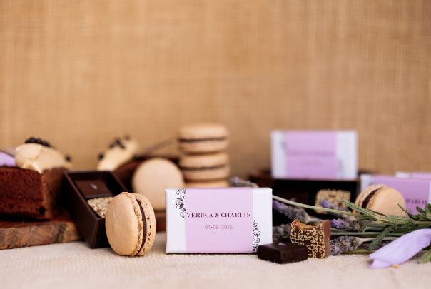 2 piece chocolate box with 'Veruca & Charlie' and date on pink sleeve on a textured surface with chocolates and macarons.