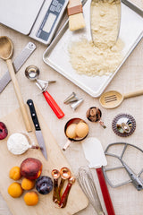 Assorted Baking utensils such as cutting boards, wooden spoons, measuringspoons, and scale on light burlap background