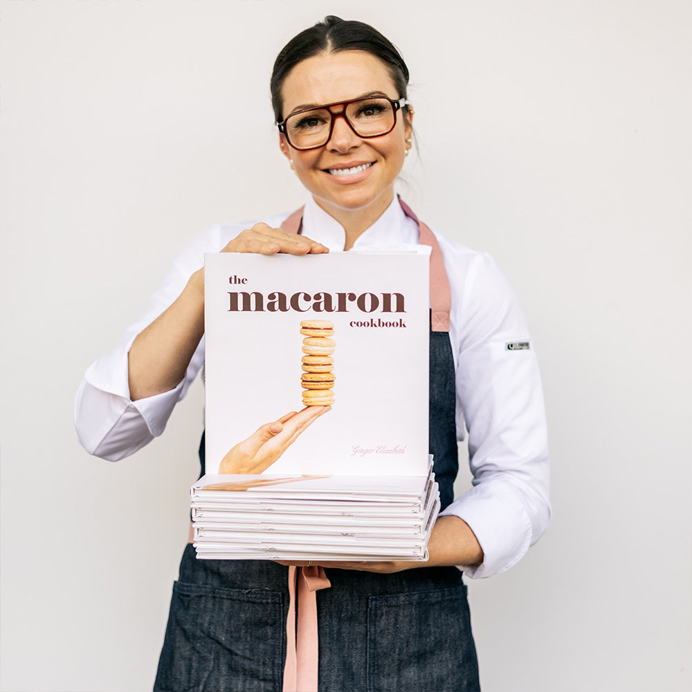 Woman holding stack of macaron cookbooks on white weekend
