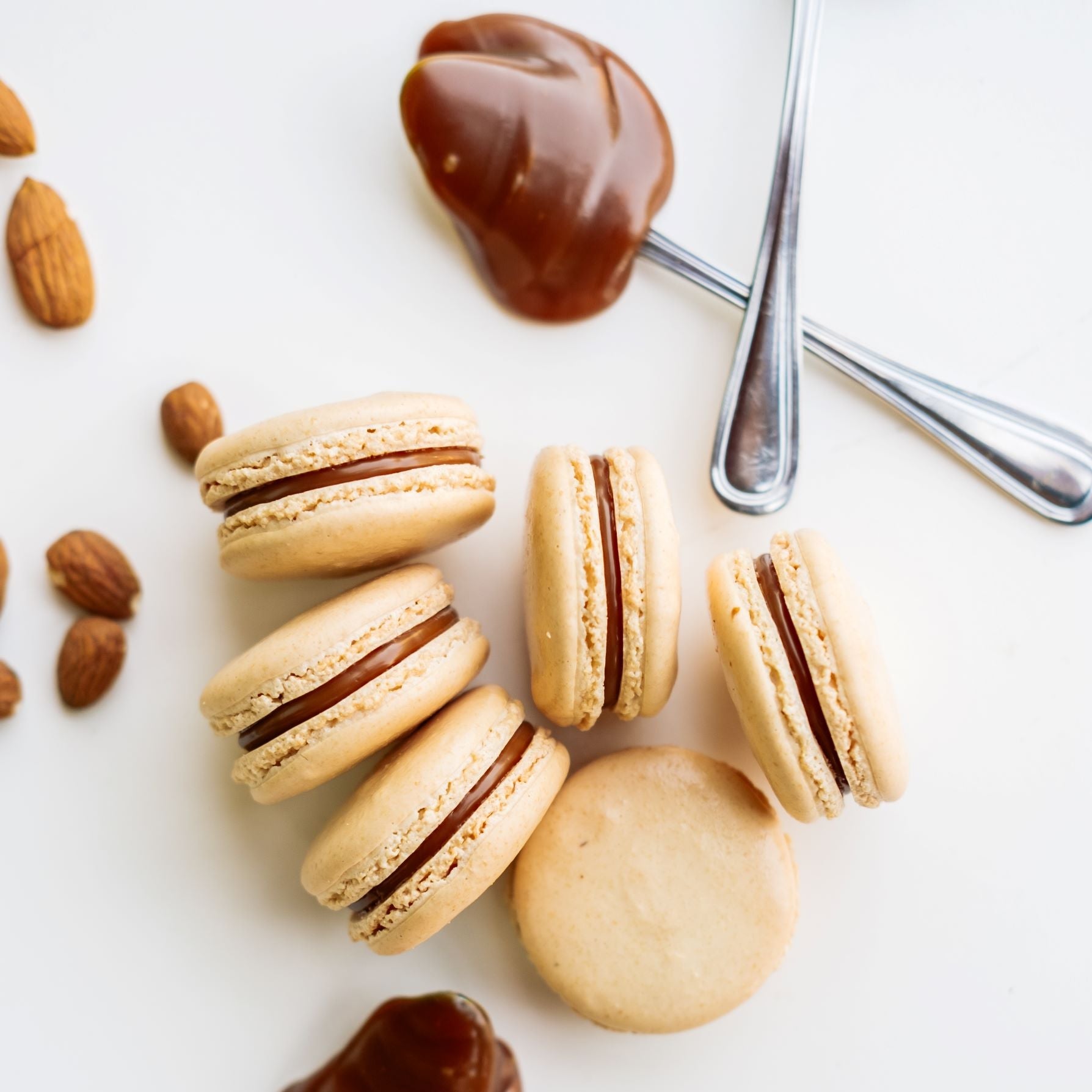 Six Salty Caramel Macarons shown with Caramel filling on spoons and scattering of fresh roasted almonds.