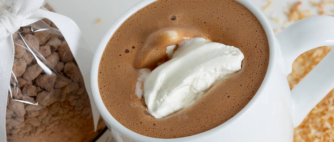 Ginger Elizabeth Chocolates Maya coconut hot chocolate in white mug and bag of hot chocolate mix on white background.