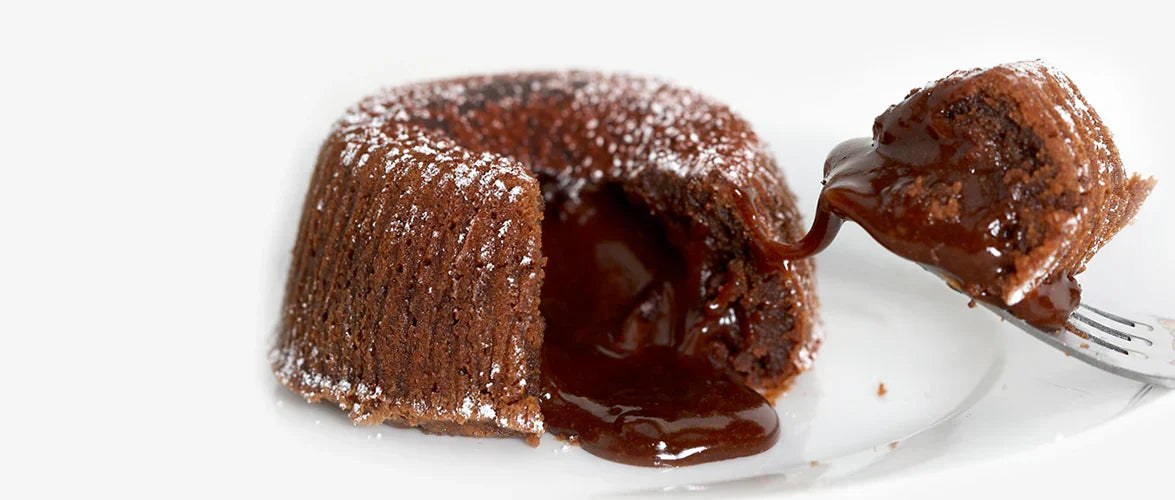 Ginger Elizabeth Chocolates chocolate molton souffle dessert on white plate with bite sized piece on fork on white background.