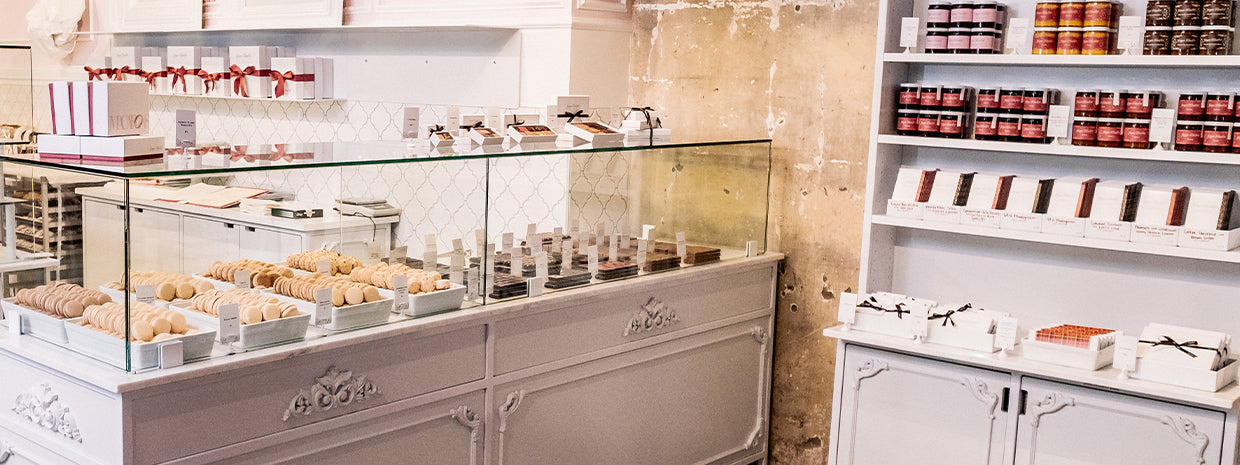 Ginger Elizabeth Chocolates interior of store with case of macaron and chocolates and hutch with sauce and jam jars, chocolate bars and boxed chocolates in foreground. 