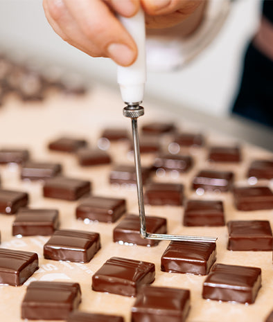 Rows of Ginger Elizabeth Chocolates chocolate bobons being stamped by hand with custom instrument. 