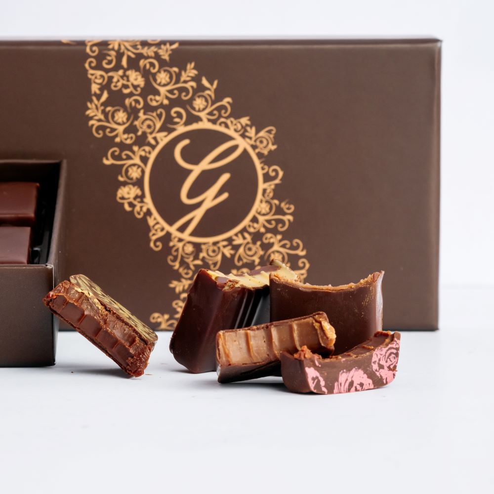 pieces of dark chocolate bonbons arranged in front of closed box on white background