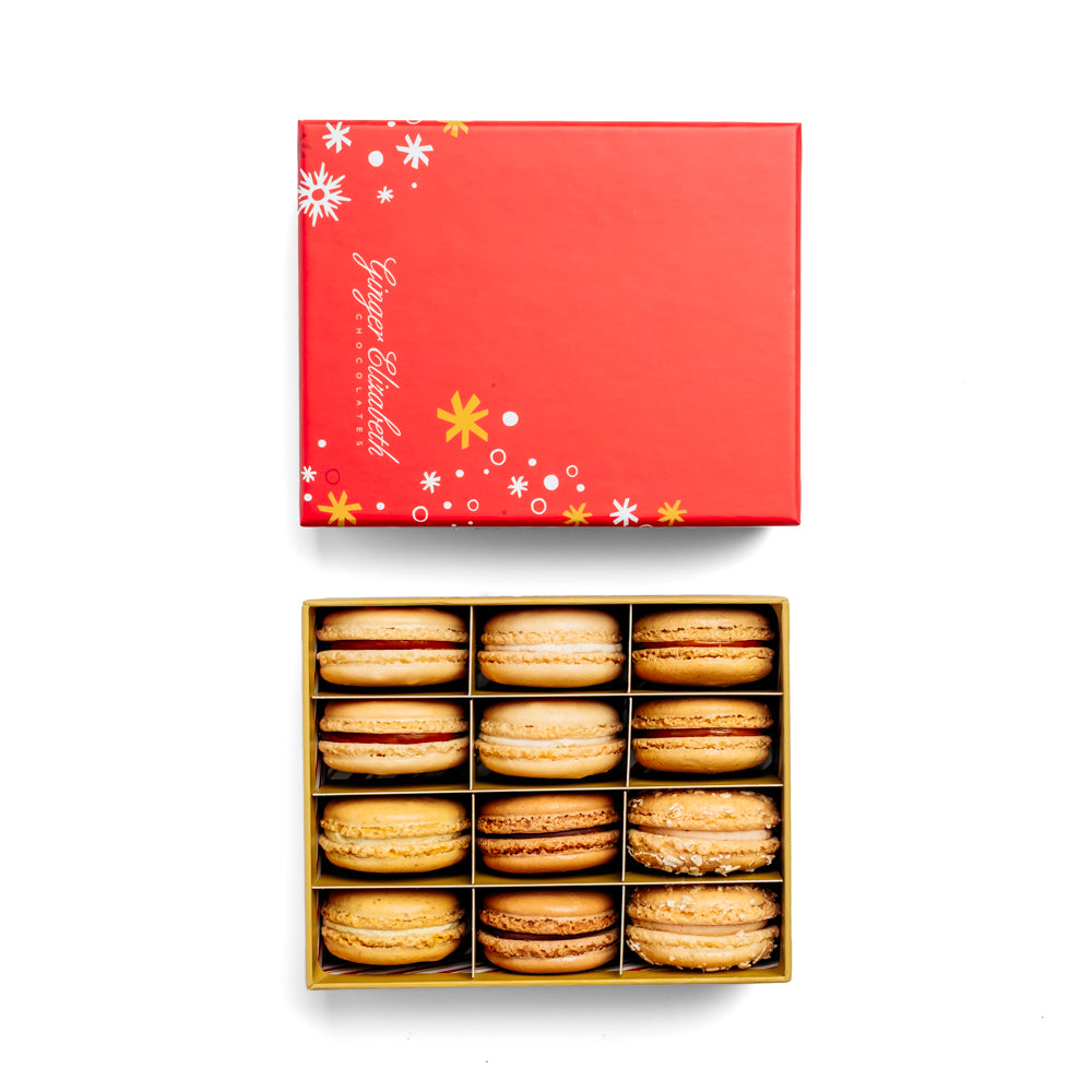 Ginger Elizabeth Chocolates open 12 Piece signature collection macaron box  with red holiday lid featuring white and gold snowflakes and stars pattern on white background.