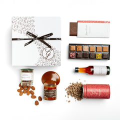 Ginger Elizabeth Chocolates Classic Gift Box including 12 piece assorted chocolate bonbon box, chocolate bar, chocolate covered almonds, classic hot chocolate tin, oaxacan spice syrup and fleur de sel caramel sauce.  All items shown with Ginger Elizabeth G filigree logo gift box with packaged items open and products spilling out except Oaxacan Spice Syrup arranged white background