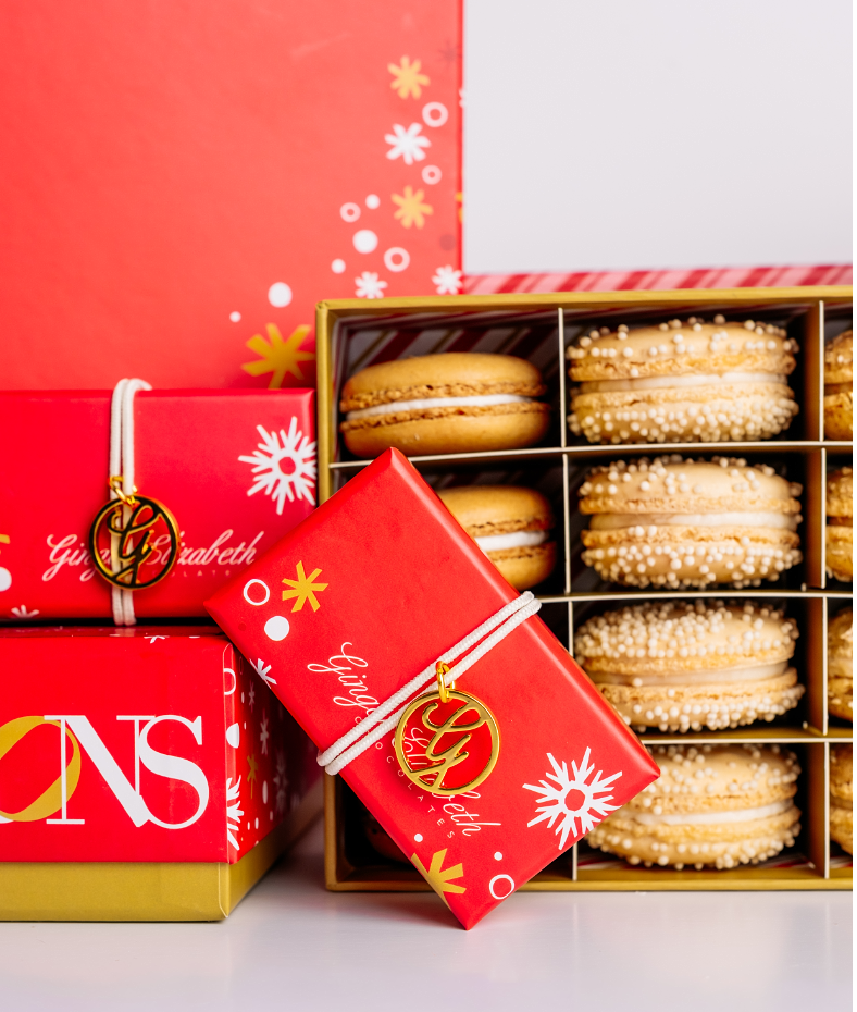 Red gift box with white text and decorative elements next to a box of macarons.