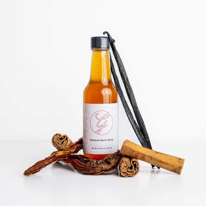Bottle of syrup with vanilla bean and cinnamon sticks on a white background