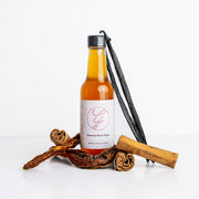 Bottle of syrup with vanilla bean and cinnamon sticks on a white background