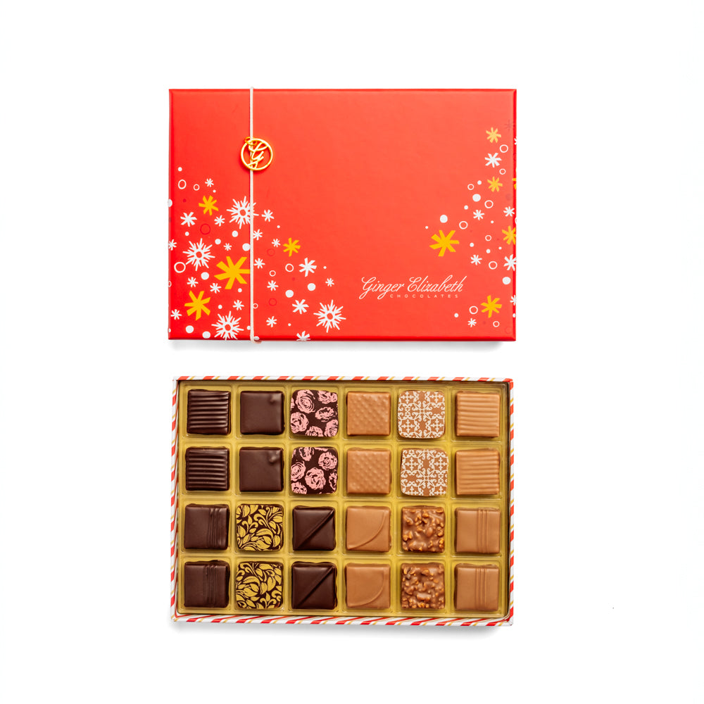 Ginger Elizabeth Chocolates open classic 24 piece chocolate box with red holiday themed lid featuring white and gold snowflakes and stars with gold G charm on white background.