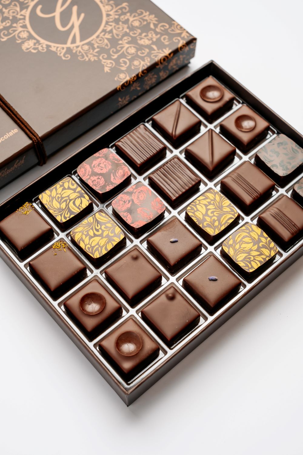 open 24-piece box of dark chocolate bonbons under closed box arranged diagonally on white background
