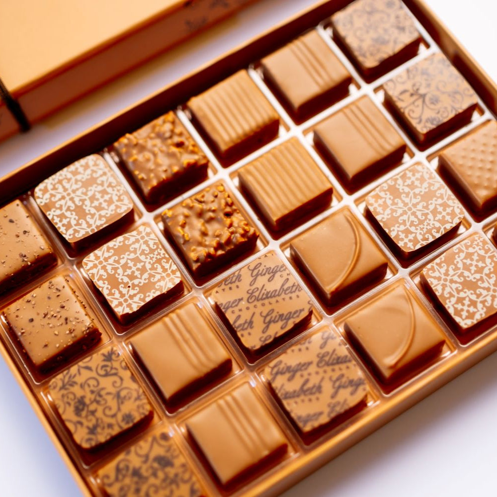 open 24-piece box of dark chocolate bonbons under closed box arranged diagonally on white background