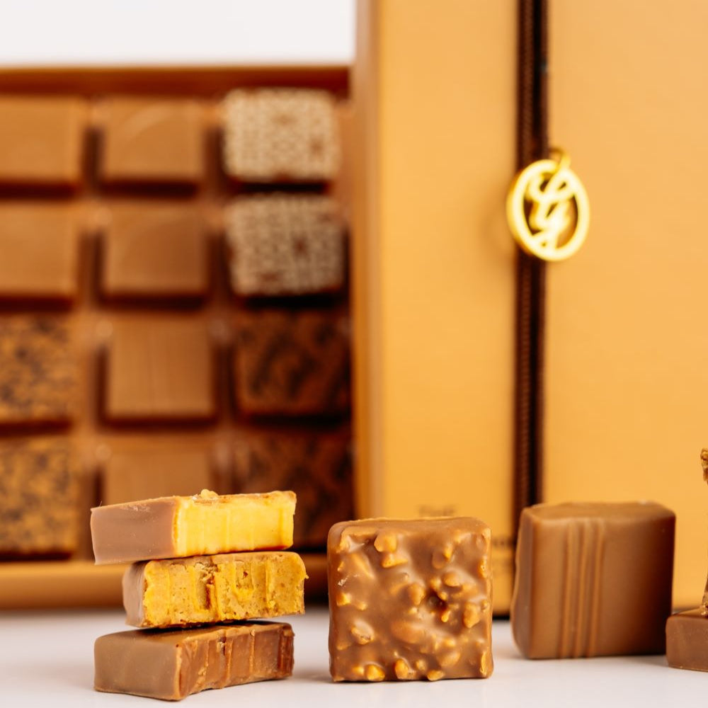 milk chocolates arranged in front of open and closed blurred boxes on white background 