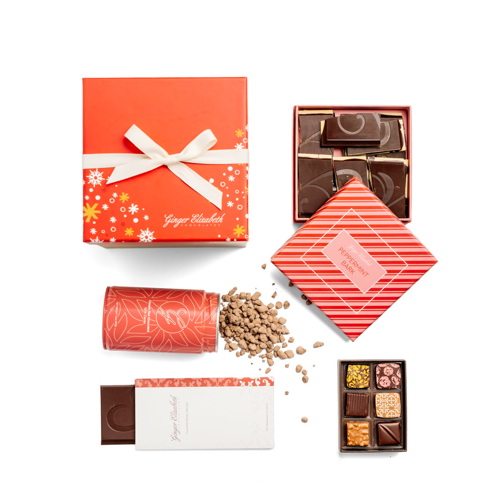 Ginger Elizabeth Chocolates holiday gift box with red lid with white and gold snowflakes and stars tied with white ribbon shown with open box of peppermint bark, classic hot chocolate tin, classic 6 piece chocolate box and chocolate bar on white background.