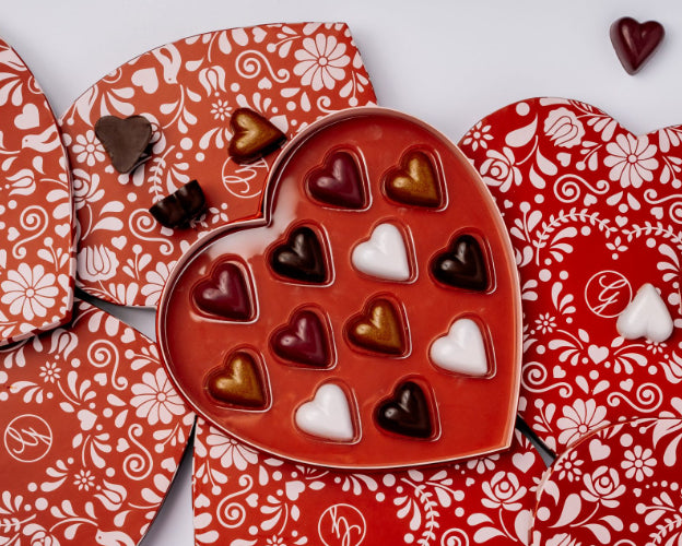 Heart shaped chocolates in heart shaped box on top of multiple boxes and loose chocolate hearts