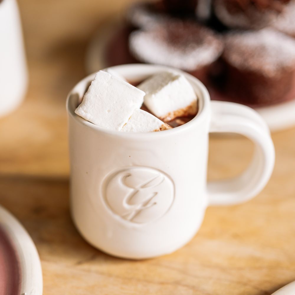 mug of hot chocolate with marshmallows and plate of brownies blurred in background