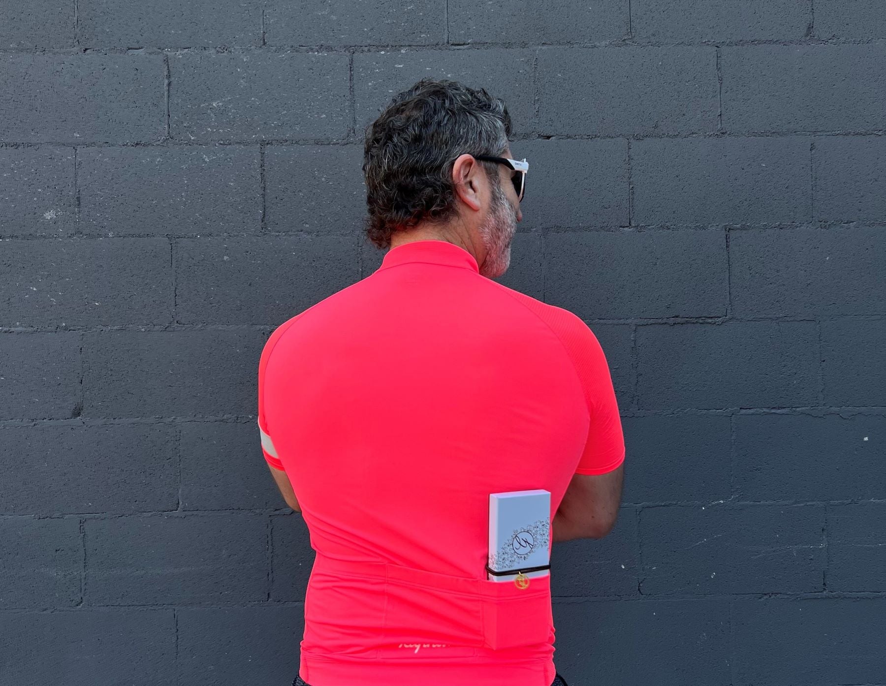 Man in red cycling jersey and sunglasses facing painted brick wall with 12pc chocolate box in back pocket