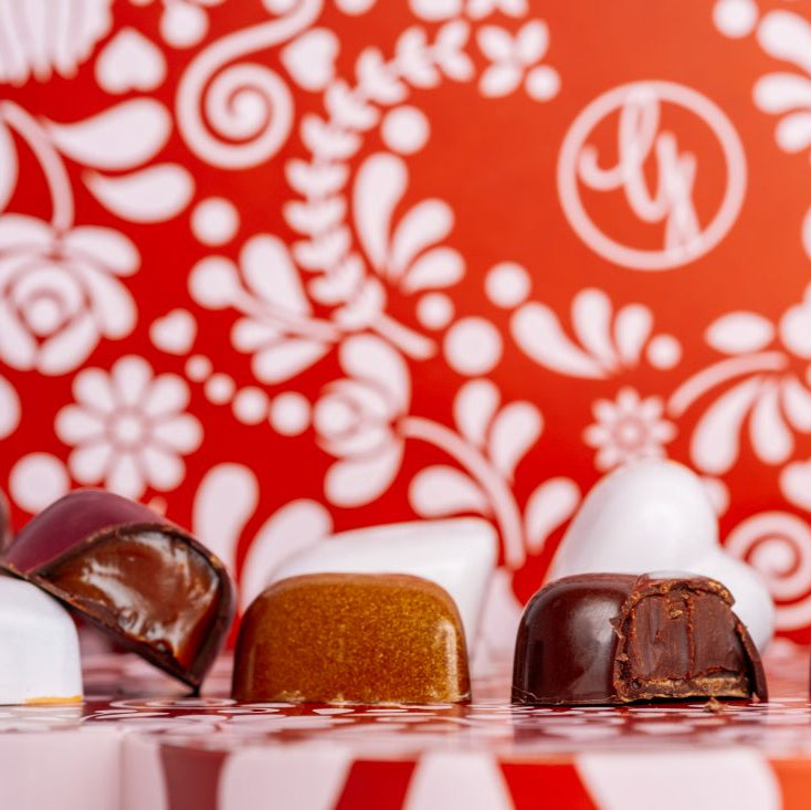 close up of Ginger Elizabeth Chocolates heart shaped bonbons with valentine floral box blurred in back ground