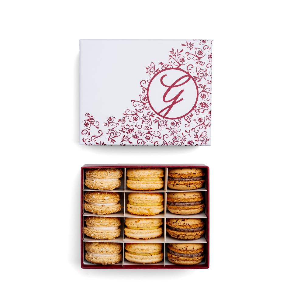 Boxed assortment of macarons with floral filigree pink G logo box lid above on white background
