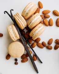 six almond vanilla macarons shown with almonds and vanilla beans on white background