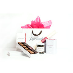 Ginger Elizabeth Chocolates Essential Gift Bag including 12 piece assorted chocolate box, chocolate dessert bar, chocolate covered almonds, classic hot cocoa tin and marshmallows. All items shown with Ginger Elizabeth white logo bag with pink tissue on white background