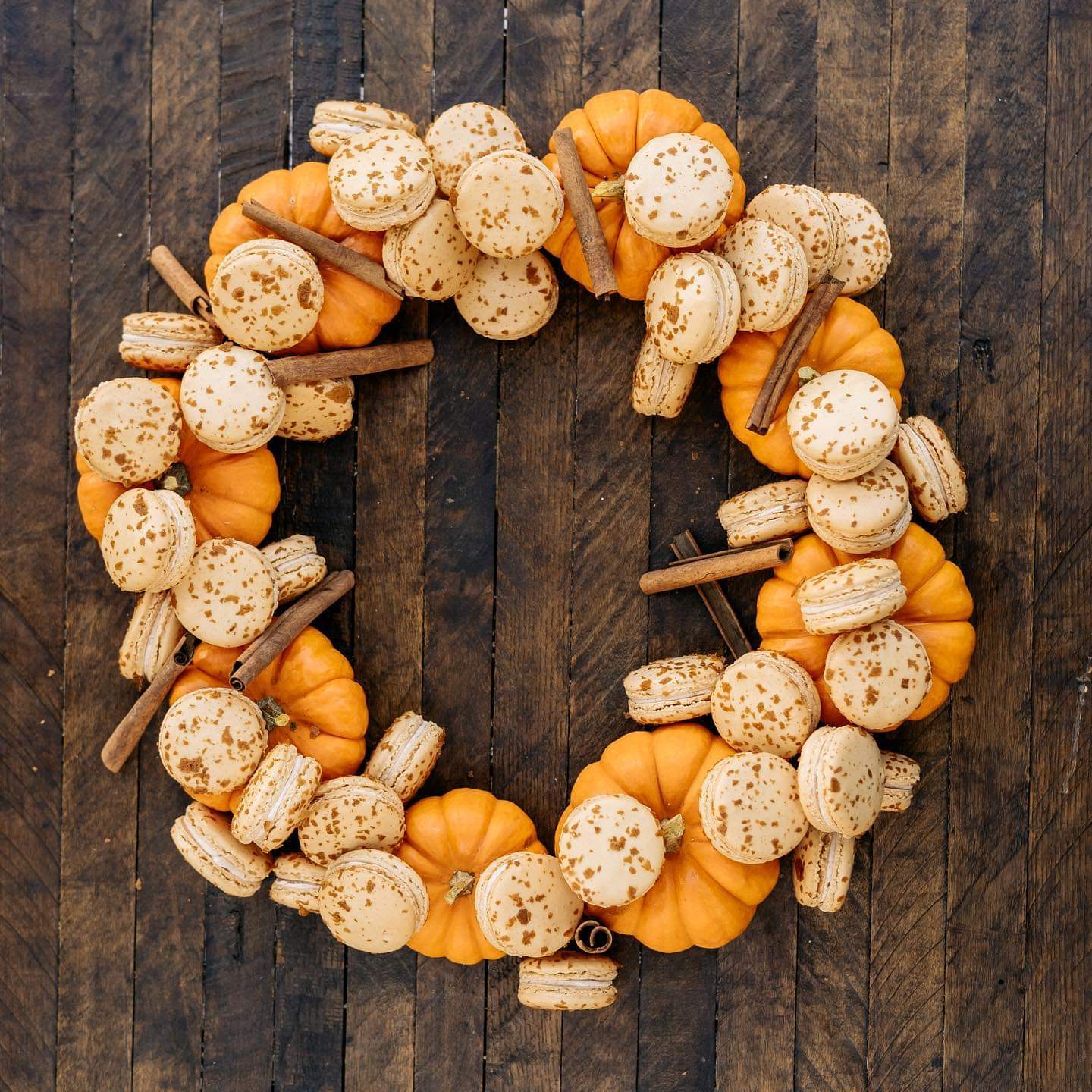 Pumpkin pie macarons with mini pumpkins and cinnamon sticks in wreath formation on dark wood background