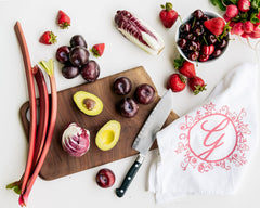 Ginger Elizabeth Chocolates logo  tea towel displayed with pink and red fruits cutting board and knife. wider image 